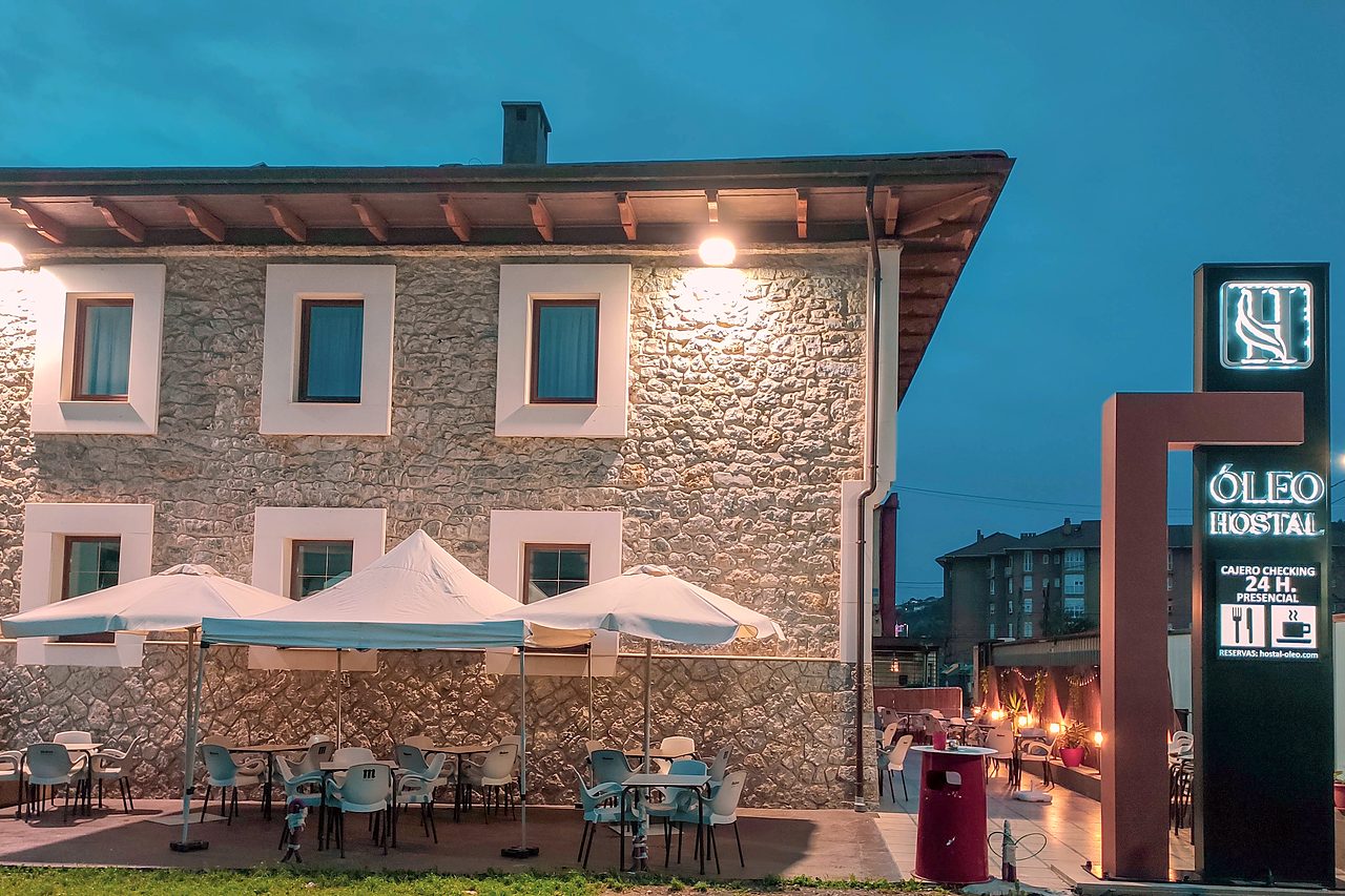 Stone facade of Hostal Óleo at dusk, with the terrace and parasols